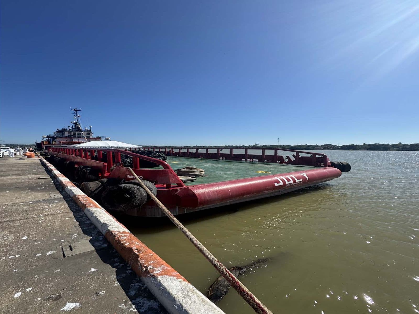 Red fuel barge JULY moored along a concrete pier at Tampico, a tug standing by astern