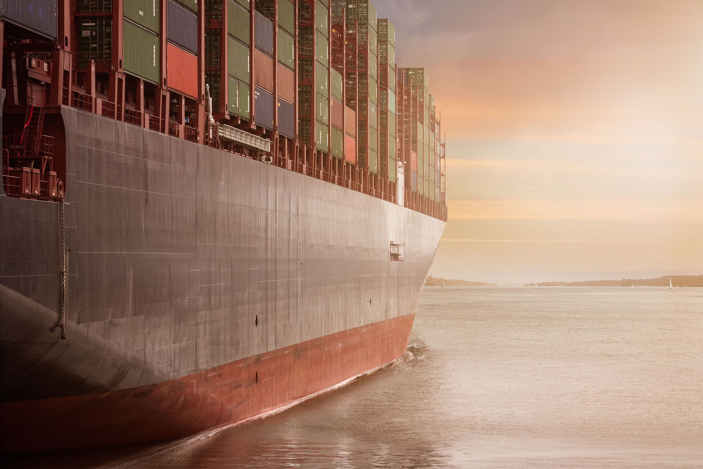 The bow of a loaded container ship under way at sunset